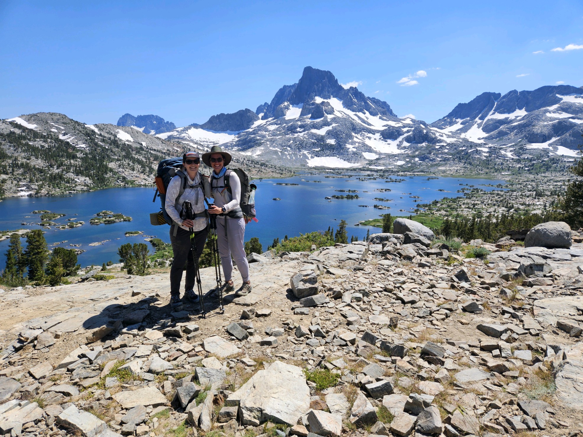 A picture of my wife and I backpacking in Yosemite. We are standing in front of a large blue lake (called Thousand Islands Lake), with some snow covered, scraggly peaks in the background.