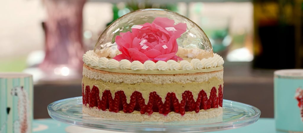 An image of Paul Hollywood's Framboisier from Season 13 of Bake Off. The cake is made of two layers of génoise sponge with a layer of crème mousseline on the inside. A layer of raspberries separates the two layers of cake. On the top of the cake there sits a clear sugar dome with a pink (candy) flower on the inside.