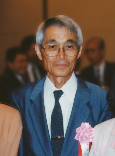 An image of the famous Japanese statistician Akaike in a nice blue suit at a formal event. Akaike appears to be older with grey hair and larger glasses.