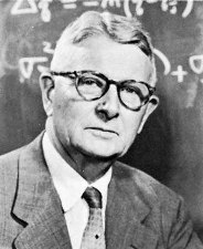 A headshot of Sewall Wright in front of a chalkboard. Sewall is a white man with small black glasses, appears to be roughly 60 in this image.
